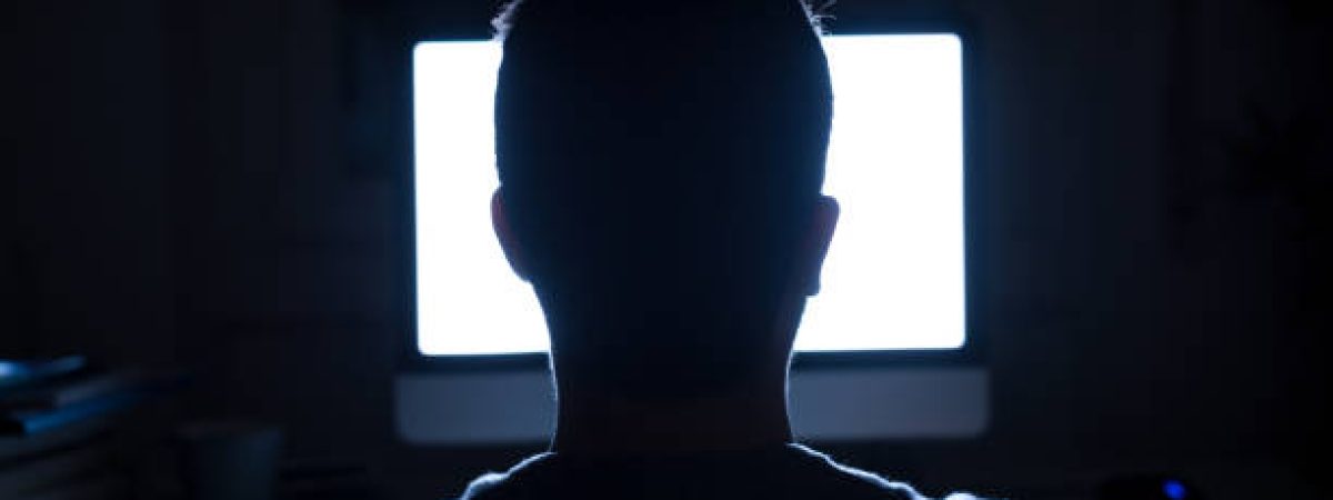 Silhouette of man's head in front of computer monitor light at night